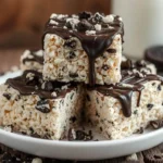 A close-up of gooey Oreo Rice Krispie Treats with crushed Oreos on top, stacked on a white plate.